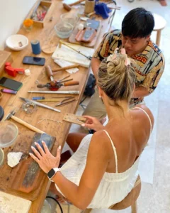 Instructor guiding a student during a hands-on jewelry-making session at the best silver class in Bali, surrounded by traditional tools and silver materials.